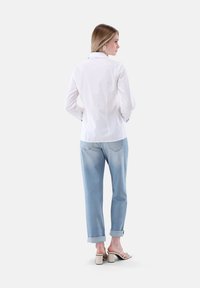 Camicia bianca con colletto, abbinata a jeans azzurri con risvoltini e sandali bianchi con tacco a blocco. Tessuto morbido, vestibilità comoda.