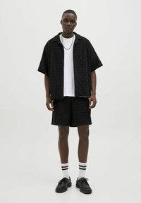 Black short-sleeve button-up shirt and matching shorts with a textured pattern. Worn over a white t-shirt, paired with black shoes and striped socks.