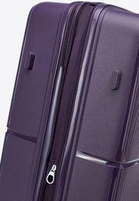 Valise rigide violette avec surface texturée, double zip et poignée latérale. Finition lisse avec des rainures verticales sur les côtés.