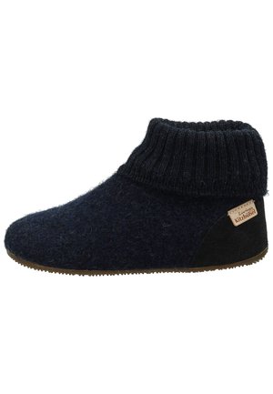 Zapatilla suave azul oscuro con puño acanalado en el tobillo, parche de tacón de ante, suela de goma y pequeña etiqueta beige que dice "Living Kitzbühel."