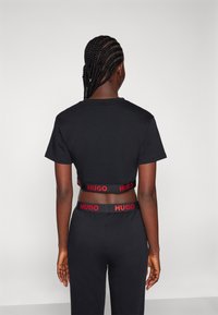 T-shirt noir court avec le logo rouge "HUGO" sur la bande élastique. Design simple, manches courtes et texture en coton lisse.