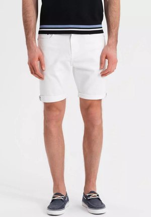 Shorts in denim bianco con orlo arrotolato e design a cinque tasche. Abbinati a scarpe da barca blu scuro e una camicia nera con strisce blu.