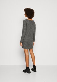 Vestido gris de punto con manga larga, textura acanalada y corte relajado, que termina por encima de las rodillas. Combinado con zapatos negros de tacón y calcetines.