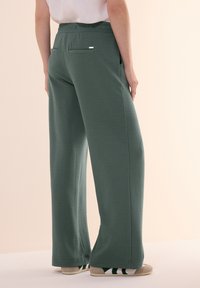 Groene gestructureerde wide-leg broek met een elastische tailleband, achterzakken en een subtiel ruitpatroon, gecombineerd met lichtgekleurde espadrilles.