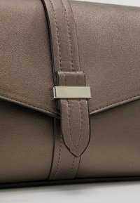 Borsa clutch in bronzo metallico con design elegante, texture liscia e chiusura decorativa in argento su una tracolla flessibile.