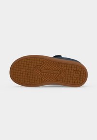 Semelle de chaussure avec une bande de roulement en caoutchouc marron à motifs de carrés et zigzags, affichant "DCSHOECOUSA" et un logo "DC" au niveau du talon.