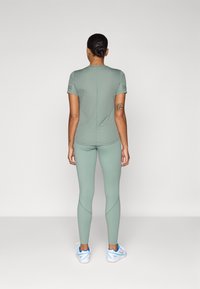 Top sportivo verde chiaro e leggings abbinati, design aderente, texture morbida, con dettagli di cucitura sottili e scarpe sportive a profilo basso.