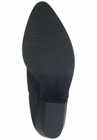 Suela de zapato negra con un agarre de goma texturizada y un acento de ante liso. El diseño tiene una ligera punta en la parte delantera.