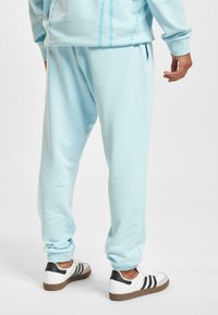 Light blue sweatpants made of soft material, featuring a relaxed fit and elastic cuffs. Paired with white sneakers with black accents.