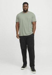 Kortærmet, olivengrøn t-shirt med "JACK & JONES" trykt i hvidt på brystet, kombineret med sorte bukser og sorte sneakers.