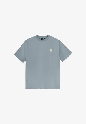T-shirt à manches courtes bleu clair en tissu doux. Présente un patch en logo carré sur la poitrine et un détail textuel sur le côté.