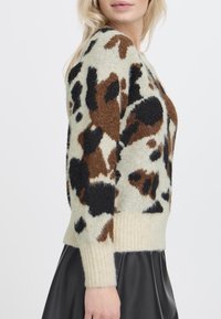 Maglione con base crema e motivi maculati marroni e neri, con polsini e orlo a costine. Realizzato in un morbido tessuto testurizzato.