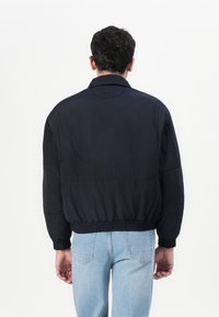 Marineblau bomberjacke mit geripptem Saum und Bündchen, verfügt über einen Kragen und ein Logo am Hals, glattes Material, lässige Passform.
