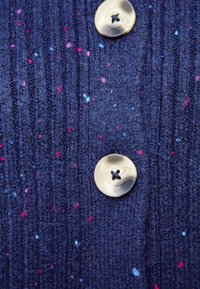 Marinblå stickad cardigan i tyg med ribbad textur och färgglada prickar. Har en rund, krämfärgad knapp med en fyrhålskonstruktion.
