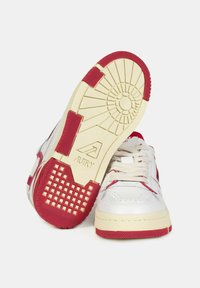 Sneakers bianchi in pelle con dettagli rossi, suola testurizzata e outsole beige. Presentano lacci e dettagli perforati sulla tomaia.