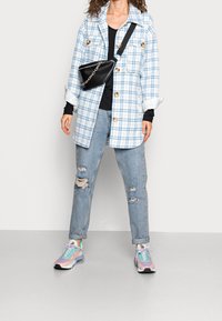 Károvaná oversize bunda v bílé a světle modré, černý top, potrhané světlé džínsy a barevné tenisky s černou crossbody taškou.