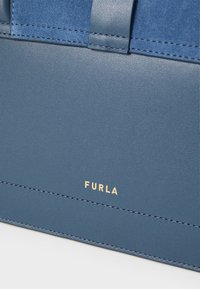 Sininen nahkainen käsilaukku, jossa on sileä pinta, rakenteellinen muotoilu, kultaiset "Furla"-logot ja kontrastiväriset mokka-akcentit kahvoissa.