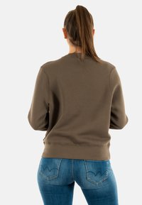 Felpa verde oliva con scollatura rotonda, polsini e orlo a costine. Abbinata a jeans blu con tasche posteriori e dettagli di cucitura.