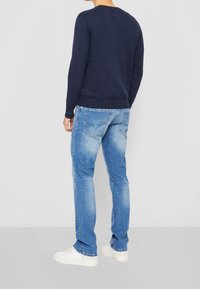 Námořnický svetr s kulatým výstřihem, úzkými manžetami a lemem, kombinovaný se světlými džínami a bílými teniskami, pohled zezadu.