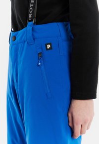 Modré vonkajšie nohavice vyrobené z odolnej látky, s bočnou zipsovou vreckom, nastaviteľným pásom a kontrastným čiernym hardvérom.