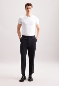 Biała, dopasowana koszulka z krótkim rękawem zestawiona z czarnymi eleganckimi spodniami, charakteryzującymi się gładką fakturą i klasycznym designem, uzupełniona czarnymi sznurowanymi butami.