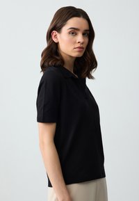 Polo shirt nero con maniche corte, realizzato in un tessuto morbido, dotato di un colletto classico e dettagli a costine lungo le maniche e l'orlo.