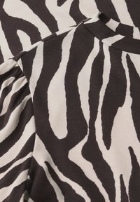 Mustavalkoinen zebra-raidallinen kangas, jossa on sileä pinta, rohkeita, aaltoilevia kuvioita ja pyöreä kaulus. Kevyt ja pehmeä.