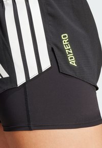 Shorts de sport noirs avec trois bandes verticales blanches, une coupe standard, et un petit logo jaune "ADIZERO" sur le côté.
