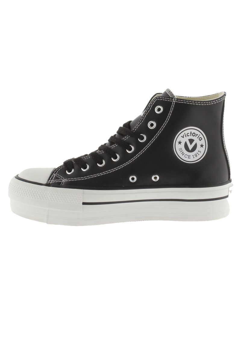 Zapatillas alta negras de material suave, con puntera y suela de goma blanca, cordones negros y un logo circular en el lateral.