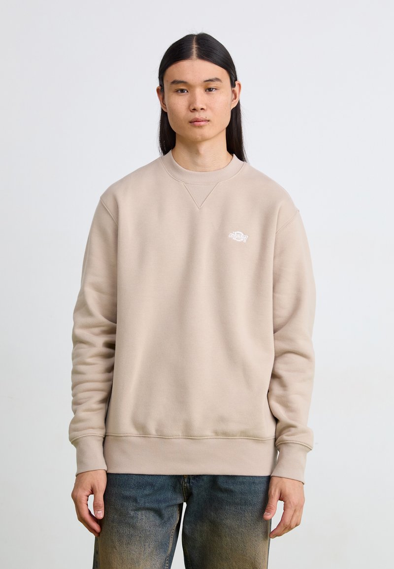 Felpa beige con collo a giro fatto di tessuto morbido, con polsini e orlo a coste, caratterizzata da un piccolo logo bianco nella parte sinistra del petto.