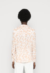 Chemise à manches longues en rose clair et blanc avec un motif abstrait. Dotée d'un col, de poignets à boutons et d'un détail de couture discret à l'arrière.