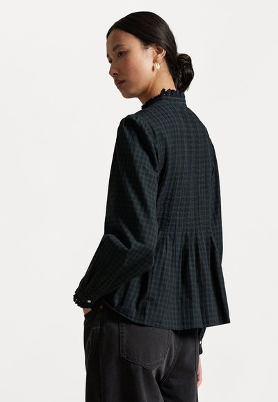 Ciemnozielona bluzka w kratę z wysokim dekoltem, plisowanym tyłem i falbaniastymi mankietami. Wykonana z miękkiego materiału o lekkiej teksturze.