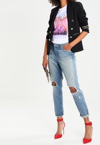 Czarny żakiet z złotymi akcentami, biały t-shirt z grafiką przedstawiającą różowe kwiaty, zniszczone jasnoniebieskie dżinsy oraz czerwone szpilki.