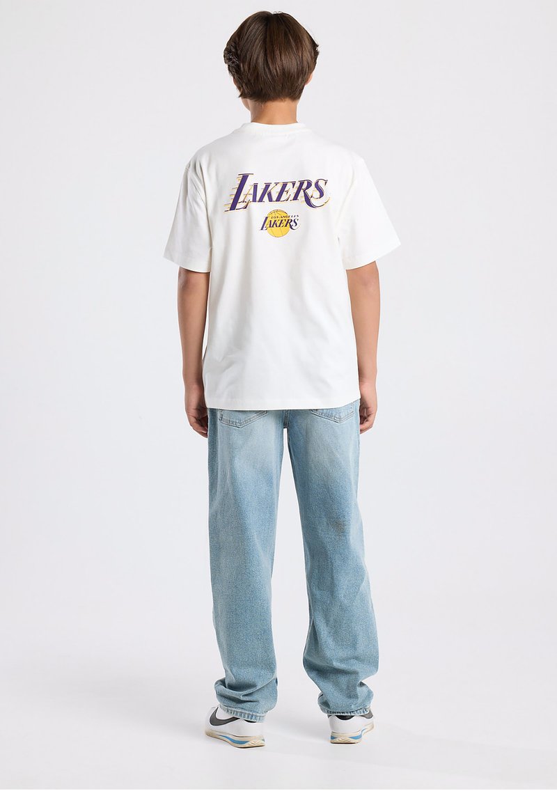 White t-shirt with "LAKERS" graphic in purple and yellow on the back, paired with loose-fitting light blue jeans and white sneakers.