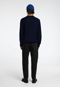 Maglione a maniche lunghe blu navy con polsini a coste, abbinato a jeans neri a gamba dritta e scarpe nere. Un berretto lavorato a maglia blu completa il look.