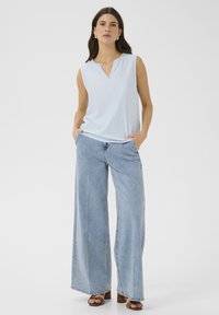 Top sans manches bleu clair avec un col en V et des coutures décoratives, associé à un jean en denim clair à jambe large et des sandales à plateforme marron.