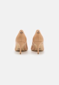 Scarpe col tacco alto in pelle color nudo con punta affusolata e design elegante. Presentano un logo metallico sul retro e un tacco sottile.