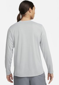 Harmaa pitkähihaisuus paita, jossa on sileä pinta, pyöreä kaula-aukko ja huomaamaton ompelu. Takana on puhdas muotoilu ilman graafisia elementtejä.