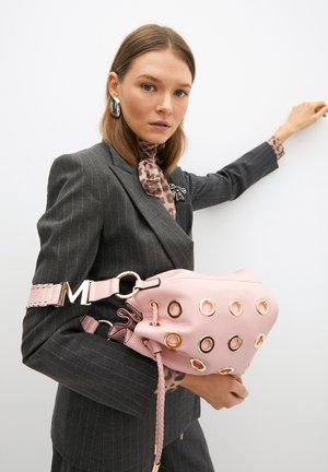 Borsa in pelle rosa con occhielli dorati rotondi, parte superiore arricciata e dettagli intrecciati. La tracolla attaccata presenta una fibbia metallica con accento "M".