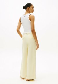 Canotta bianca a costine abbinata a pantaloni larghi giallo chiaro con due tasche sul retro. Tessuto liscio, vestibilità sartoriale e silhouette pulita.