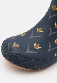 Bottine imperméable avec un fond bleu marine orné d'un motif floral jaune et marron. Semelle en caoutchouc noire texturée et finition brillante.