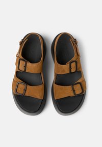 Bruna mockaskinnsandaler med två justerbara remmar och svarta gummisulor. Har metalspännen och en texturerad innersula.