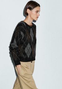 Maglione argyle nero e grigio in una morbida e pelosa texture, con scollatura rotonda e polsini a coste, abbinato a pantaloni beige a vita alta.