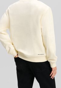 Felpa color crema con polsini e orlo a costine, caratterizzata da un discreto dettaglio del logo nella parte bassa della schiena. Texture morbida e vestibilità rilassata.