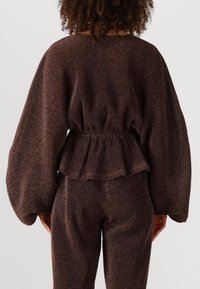 Bruine textuur bijpassende set met een peplum top met klokmouwen en aansluitende broek, met ribbel details door het geheel.
