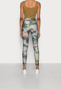 Mönstrade leggings med blommor i nyanser av grön, kräm och persika, med hög midja; ihop med en brun linne och vita sneakers.