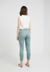 Pantalones ajustados en azul claro con piernas ajustadas, de longitud recortada y dos bolsillos traseros. Combinados con una blusa sin mangas blanca y sandalias.
