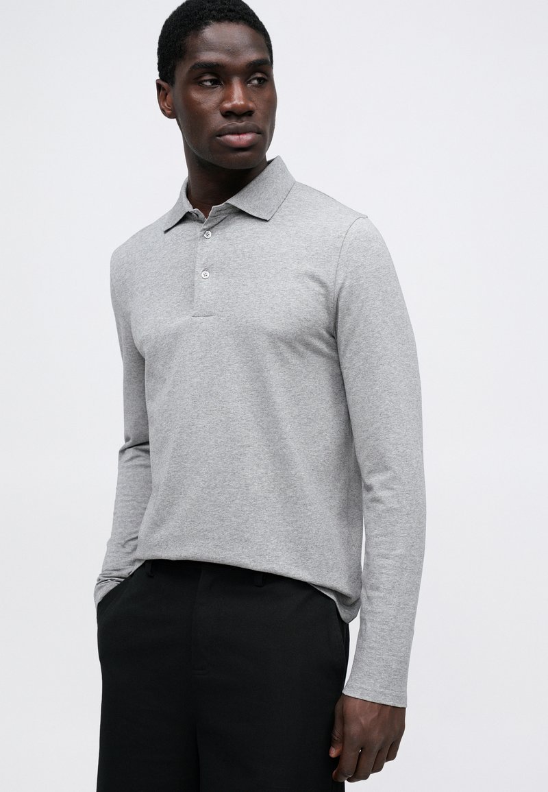 Polo shirt grigio a maniche lunghe con colletto, placket a due bottoni e vestibilità relaxed. Tessuto liscio e dettagli di cucitura sottili.