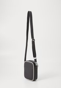 Black crossbody bag with a textured surface, square shape, white piping, adjustable strap, and side perforations for ventilation.