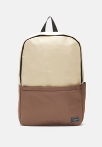Zaino beige e marrone realizzato in tessuto resistente, dotato di un ampio compartimento principale, tasca frontale, cerniera nera e maniglia superiore per il trasporto.